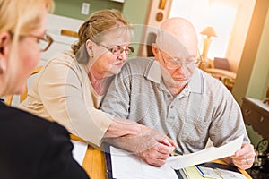 Attentive Senior Adult Couple Going Over Documents in Their Home with Agent At Signing