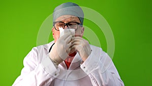 Senior adult doctor, caucasian nationality, in white coat, takes off his medical mask and coughs, hiding behind napkin