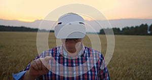 Senior adult farmer in a virtual reality helmet in a field of grain crops. In the sunset light, an elderly man in a