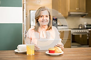 Senior adult having breakfast holding a tablet