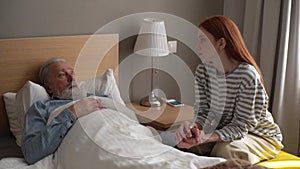 Senior adult male sickness patient lying on bed in recovery room at hospital with granddaughter looking after.