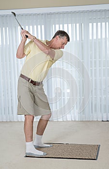 Senior adult man practicing golf grip and swing in bedroom