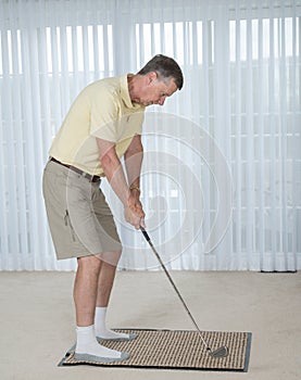 Senior adult man practicing golf grip and swing in bedroom