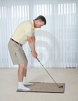 Senior adult man practicing golf grip and swing in bedroom