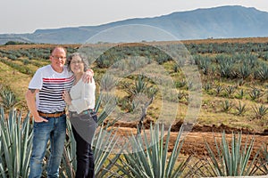 Senior adult tourist couple smiling against an agricultural landscape of blue mexican agave