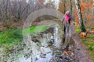 Senior adult woman walking with her dog on bank of a hiking trail flooded with rainwater