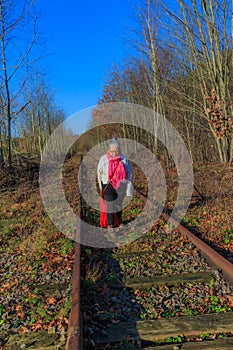Senior adult woman walking on train tracks with head down thoughtful and sad