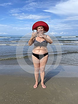 Senior adventure is ageless woman wearing in swimsuit speak by mobile phone on the beach. Summer vacation for pensioner