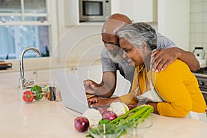 Senior african american couple cooking together in kitchen using laptop