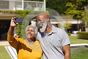Senior african american couple spending time in sunny garden together taking selfies and smiling