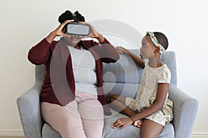 Senior african american grandmother sitting on couch wearing vr headset beside smiling granddaughter