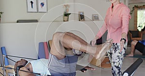 Senior african american man exercising in pilates class with female coach, unaltered, in slow motion