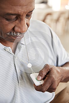 Senior African American  man pushing an assistance alarm which heï¿½s wearing around his neck, close up, vertical