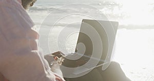 Senior african american man sitting and using laptop on sunny beach