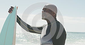 Senior african american man standing with surfboard on sunny beach