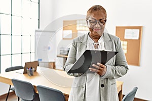 Senior african american woman business worker writing on clipboard at office