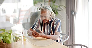 A senior African American woman is focused on her smartphone at home, taking medicine