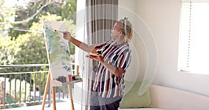 A senior African American woman paints on canvas at home, focused on her artwork