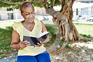Senior african american woman reading book sitting on the bench at the park