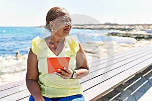 Senior african american woman using touchpad sitting on the bench at the beach