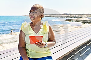 Senior african american woman using touchpad sitting on the bench at the beach