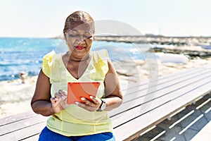 Senior african american woman using touchpad sitting on the bench at the beach