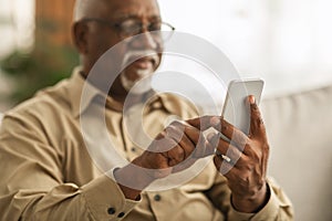 Senior African Man Using Smartphone Texting Sitting On Sofa Indoor
