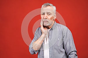 Senior aged man suffering from toothache on red background