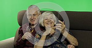 Senior aged man and woman sitting together on a sofa. Working on smartphone