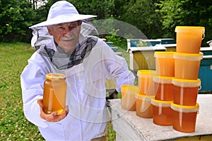 Senior apiarist presenting jar of fresh honey in apiary