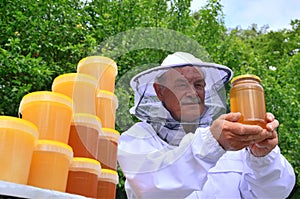 Senior apiarist presenting jar of fresh honey in apiary