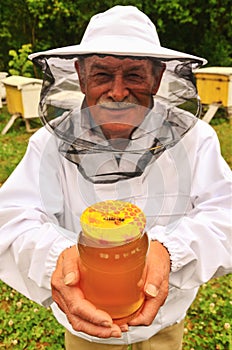 Senior apiarist presenting jar of fresh honey in apiary