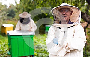 Senior apiarist in protective suit standing in bee yard