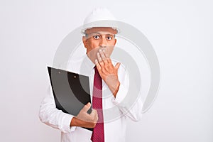 Senior architect man wearing security helmet holding clipboard over isolated white background cover mouth with hand shocked with