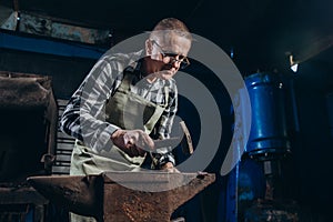 Senior an artisan blacksmith knocks with a hammer on iron to shape