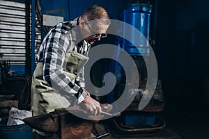 Senior an artisan blacksmith knocks with a hammer on iron to shape