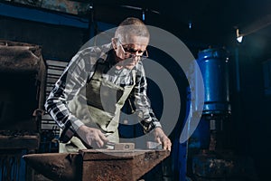 Senior an artisan blacksmith knocks with a hammer on iron to shape