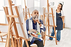 Senior artist man at art studio asking to be quiet with finger on lips