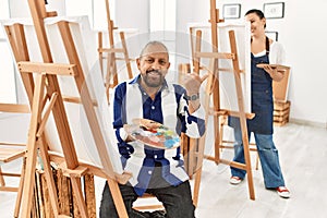 Senior artist man at art studio pointing to the back behind with hand and thumbs up, smiling confident
