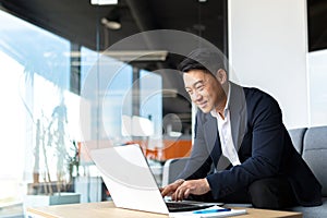 Senior Asian business man working on laptop online, smiling and rejoicing, happy boss business owner working in office