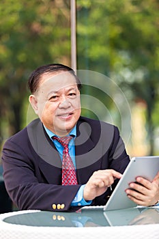 Senior Asian businessman in suit using tablet PC