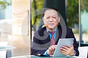 Senior Asian businessman in suit using tablet PC