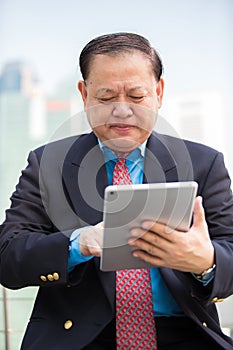 Senior Asian businessman in suit using tablet PC