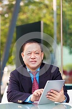 Senior Asian businessman in suit using tablet PC