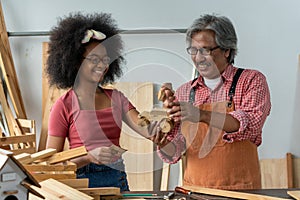 Senior Asian carpenter teaching a girl to work with wood in carpentry shop