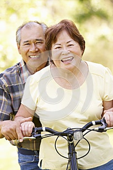 Senior Asian couple both sitting on one bike in park