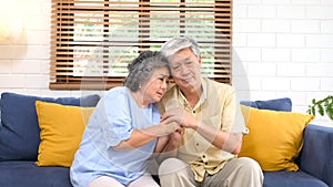 Senior asian couple comforting each other from depressed emotion while sitting on sofa at home living room, old retirement
