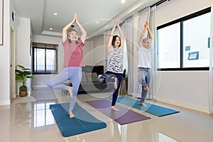 Senior asian couple and daughter are doing workout at home in standing yoga balancing pose for relaxing exercise and elder healthy