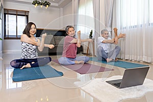 Senior asian couple and daughter are exercising at home doing sitting meditation yoga pose with online trainer class from internet