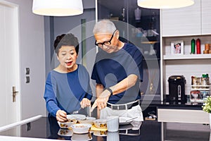 Senior Asian couple grandparents cooking together while woman is feeding food to man at the kitchen. Long lasting relationship